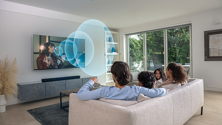 Rodzina ogląda telewizję w salonie; na ekranie kobieta śpiewa, a z telewizora emitowane są fale dźwiękowe, ilustrujące funkcję Acoustic Center Sync